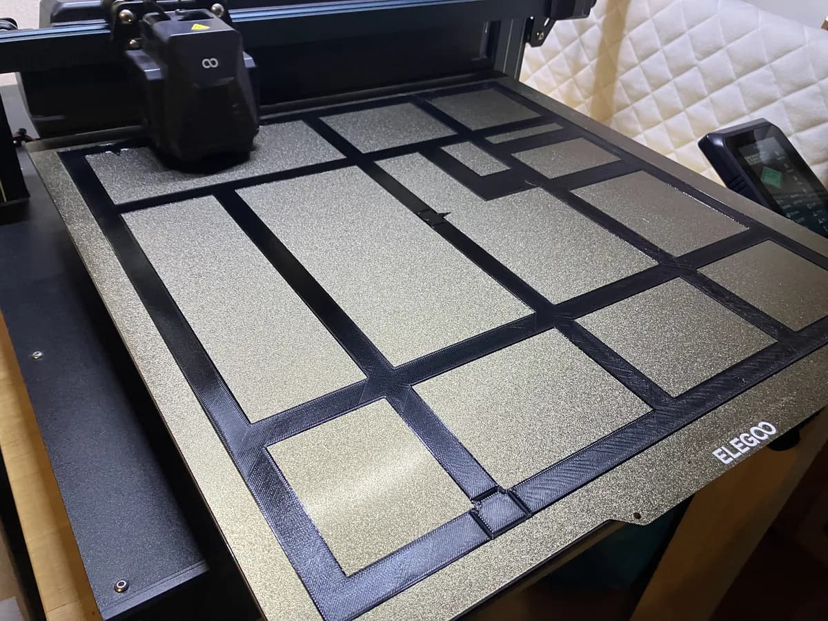 Das Druckbett eines 3D-Druckers mit einem frisch gedruckten schwarzen Rahmen aus vielen Fächern.